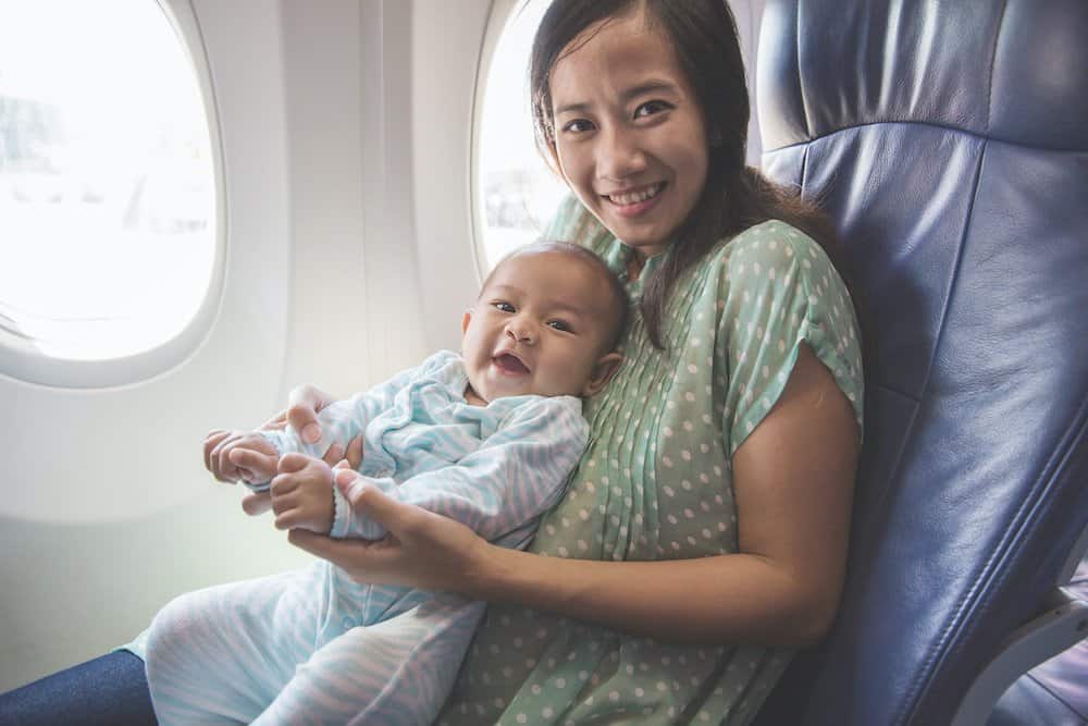 Happy mother and baby sitting together in airplane cabin near window