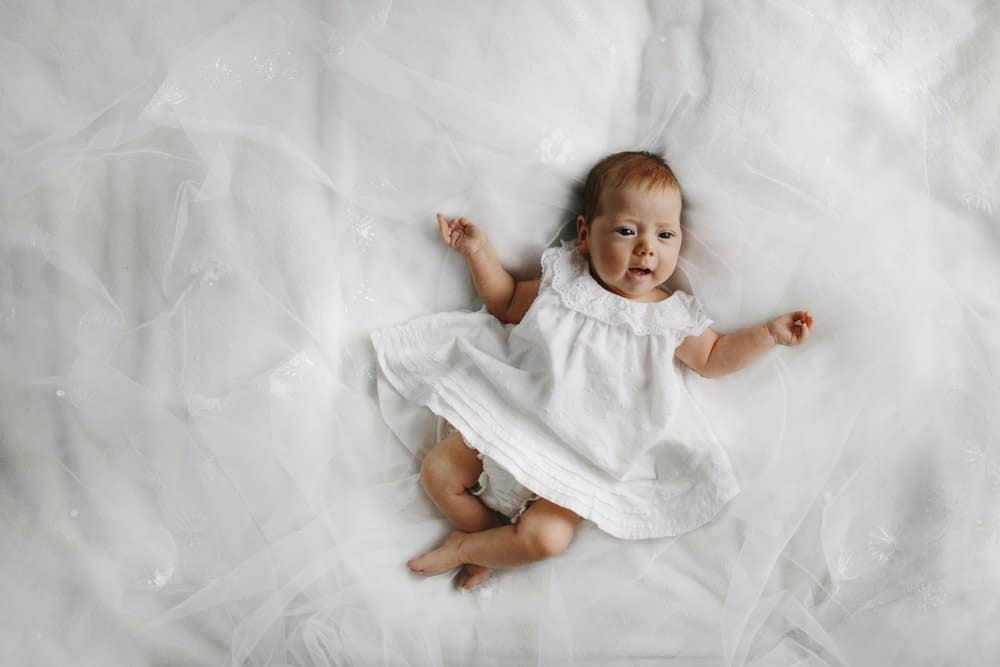 Adorable newborn baby girl in a white dress lies on a bed