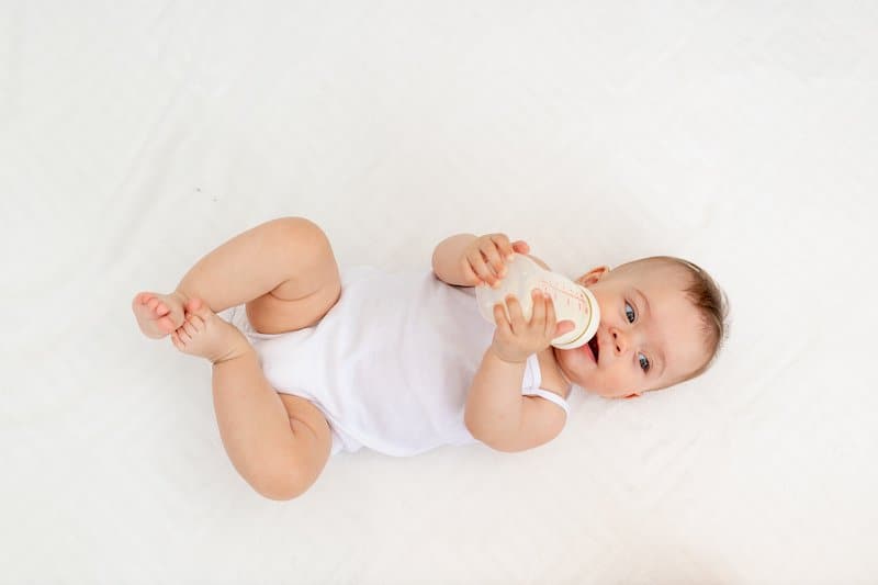 An infant baby is laying on her back and drinking milk from a bottle.