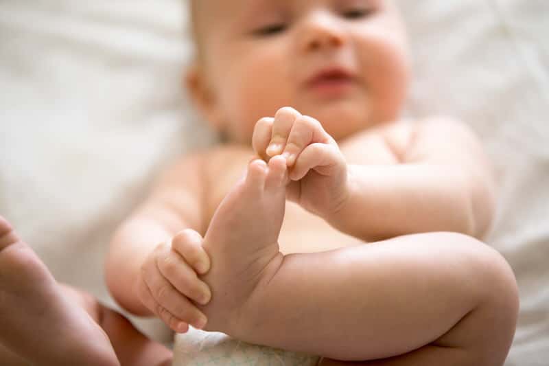 Baby finding interest in his feet and rubbing them together.