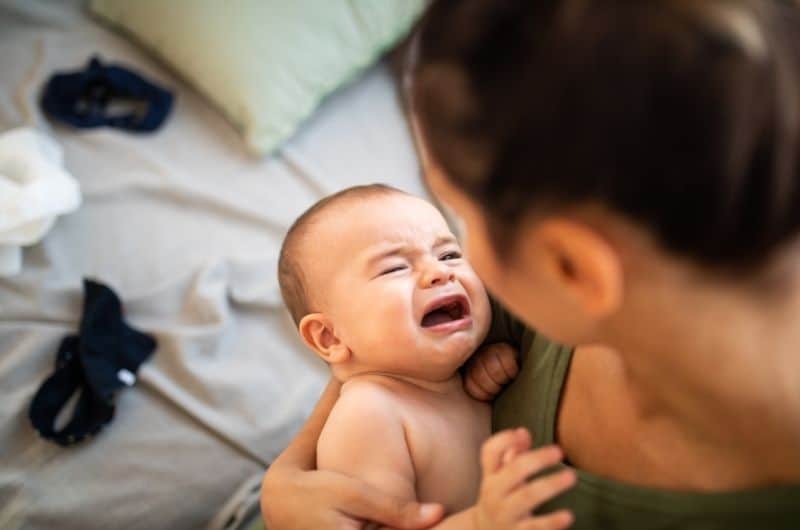 An unhappy baby with his mom. Symptoms to look out for if your baby has a smelly poop.