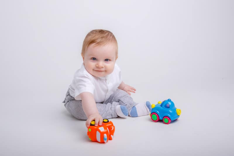 With the help of doing some regular activities, a baby boy is now able to sit up on his own and is playing with his toy cars.