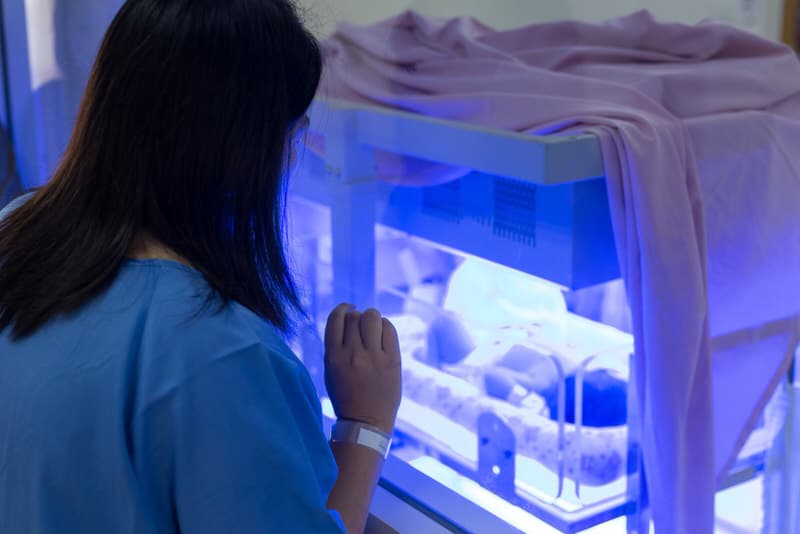 A mom is looking at her newborn baby getting light therapy treatment done for jaundice.