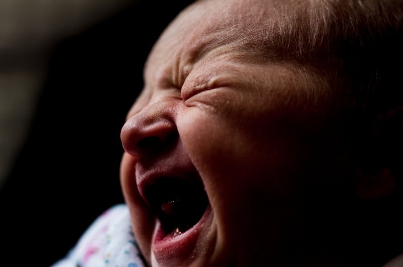 A newborn baby is crying at night because of gas trapped in his body, a risk that happens during dream feedings.