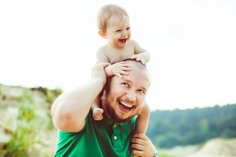 A dad is bonding with his infant son by playing with him outside. They're both happy and laughing.