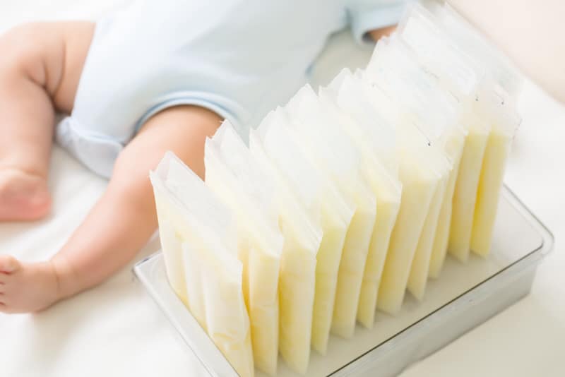 A newborn baby is laying down next to stacks of frozen breast milk, that mom has chosen to pump and freeze for future feedings.