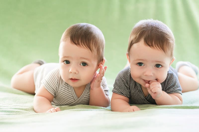 Two adorable twin boys are happily practicing tummy time.
