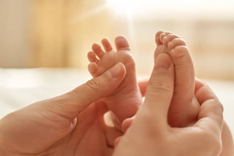 A mom is massaging her newborn baby's feet with baby oil.