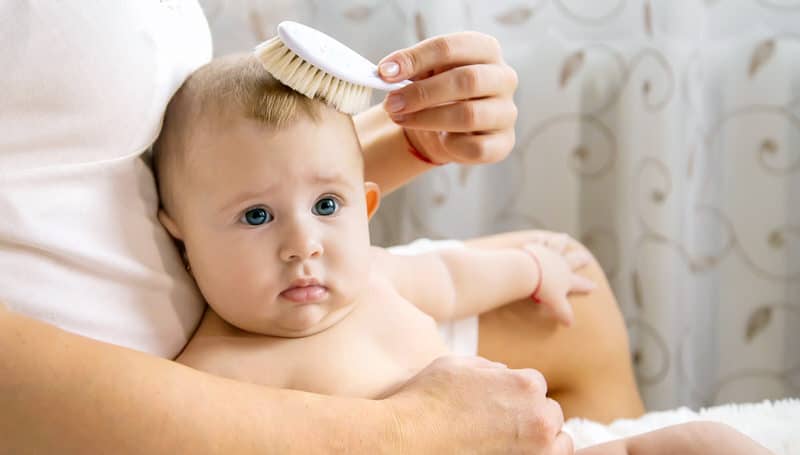 A mom is brushing her baby boy's hair, using it instead of a comb to be gentle on her son's cradle cap.