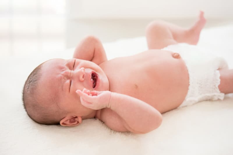 A newborn boy is crying while laying down in his crib.