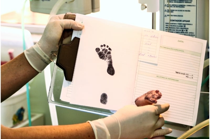 A newborn baby is getting his footprint taken by a nurse, shortly after birth.