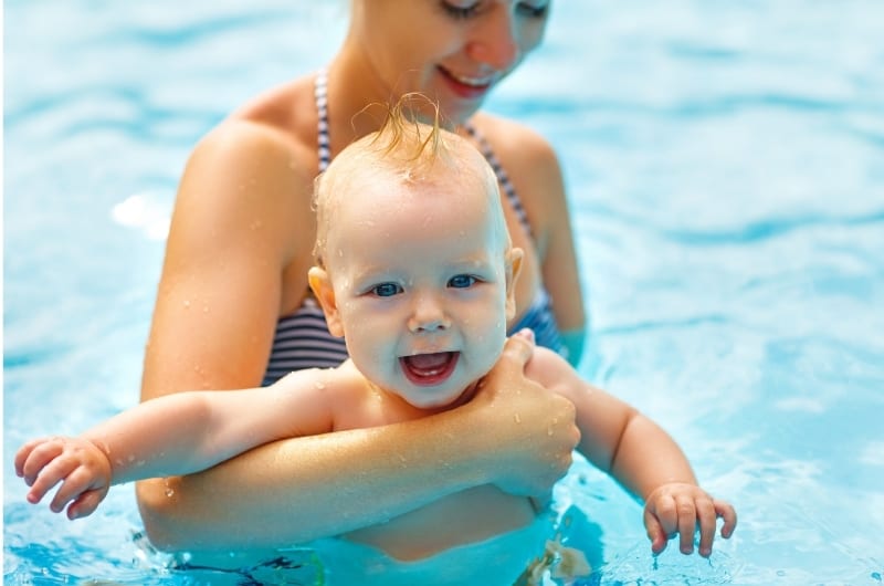 Mom is teaching her infant son how to swim in a pool.