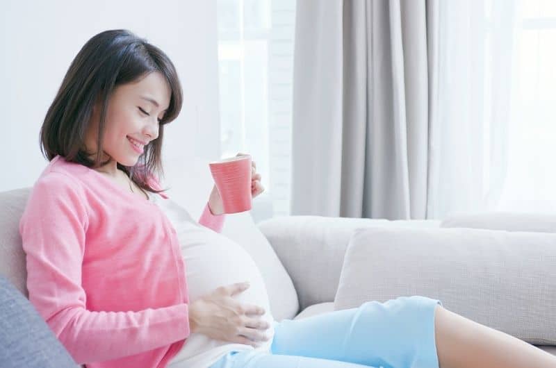 A 39 weeks pregnant woman is laying down on the sofa drinking cumin tea.