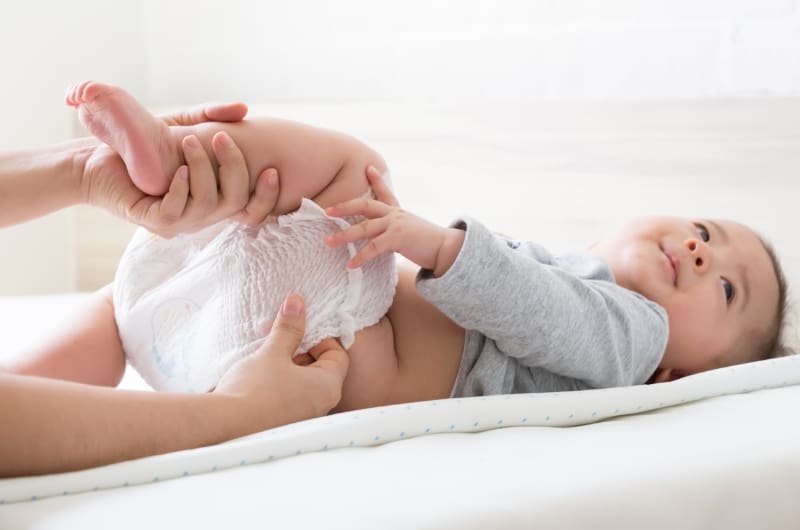 Mom is changing her infant son's diaper because his diaper tabs ripped again.