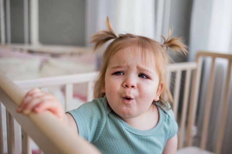 An infant girl is crying and hiccuping at the same time in her crib.
