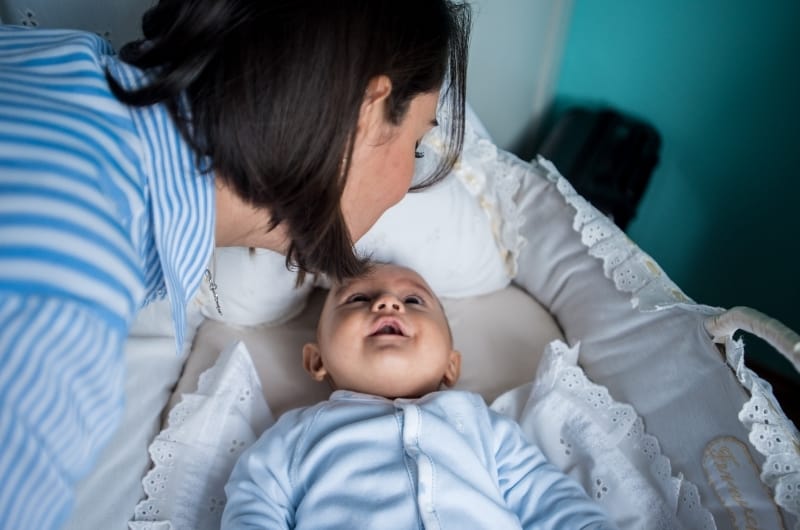 An infant boy, who was crying in his crib before, is now happy to see his moms face next to him.