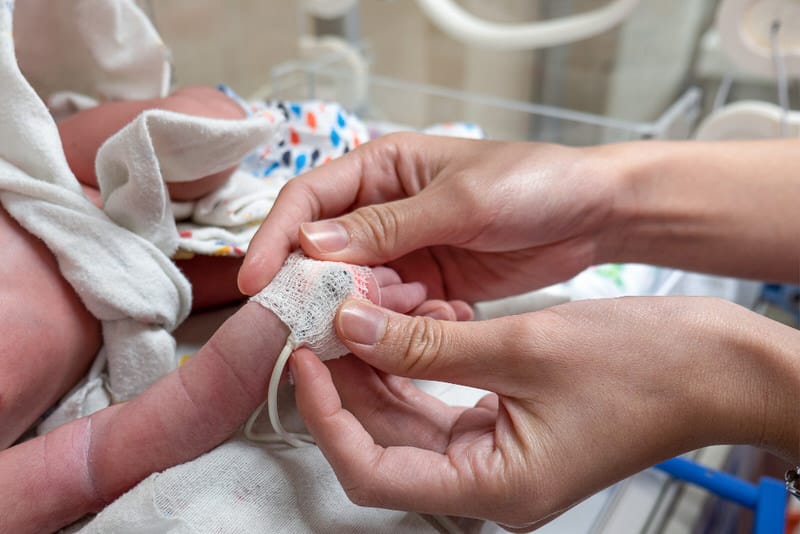 A newborn baby is getting cared for after birth by a nurse. The nurse is attaching a pulse monitor to the newborn's right hand.