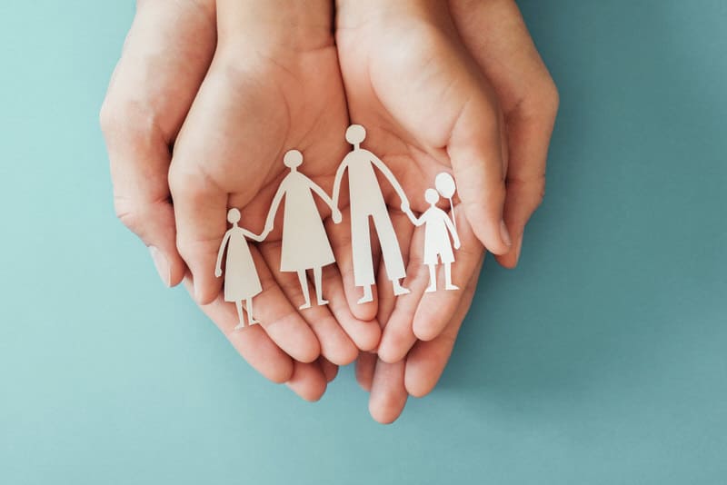 A cutout of a paper family is laid out on 2 parents' hands.