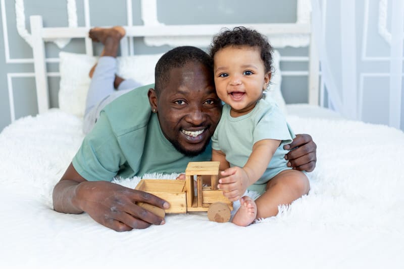 Dad and his infant daughter are hanging out and playing on the bed.