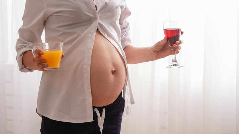 A pregnant woman is holding a glass of orange juice as well as a glass of wine.