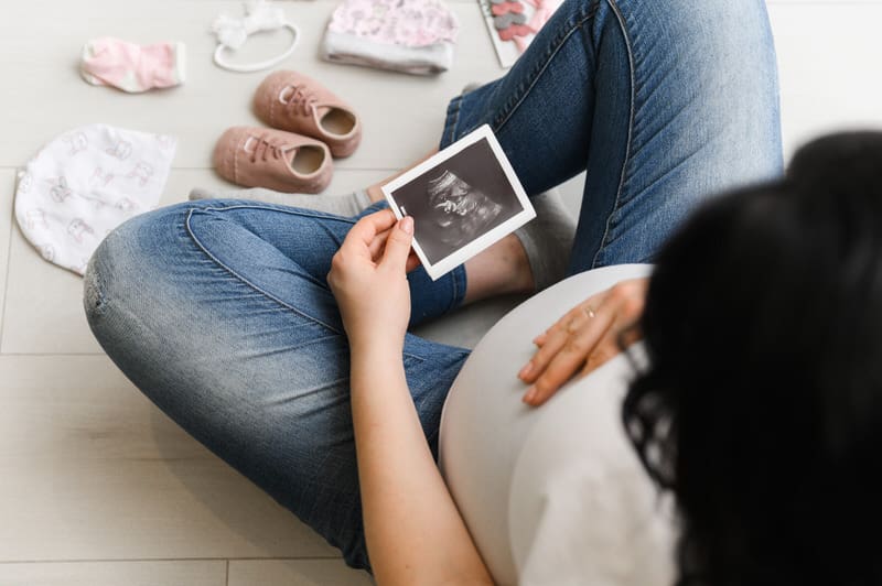A young pregnant woman is sitting down and looking at her recent ultrasound picture.