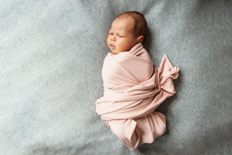 A newborn baby is comfortably laying down in his swaddle position.