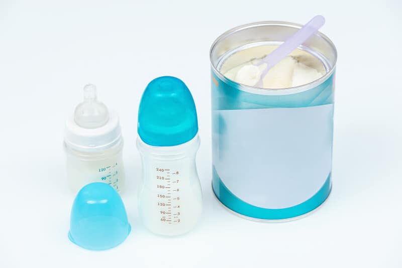 A baby formula container next to a baby bottle.