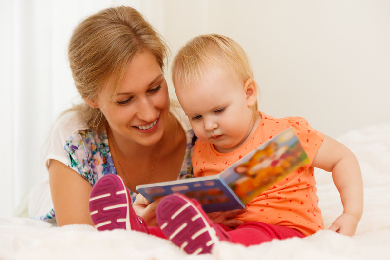 Mom is helping stimulate her toddler by reading books to her and showing her visual imagery.
