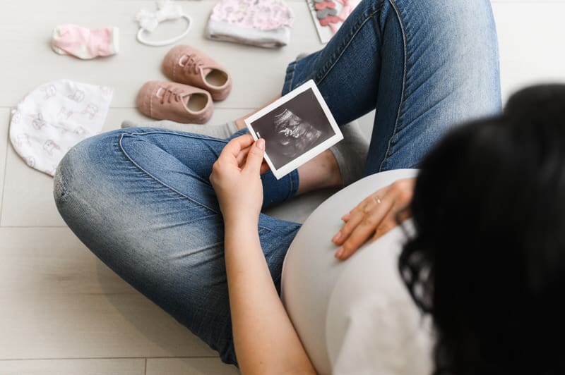 A pregnant woman is sitting down and looking at her recent ultrasound picture of her baby.