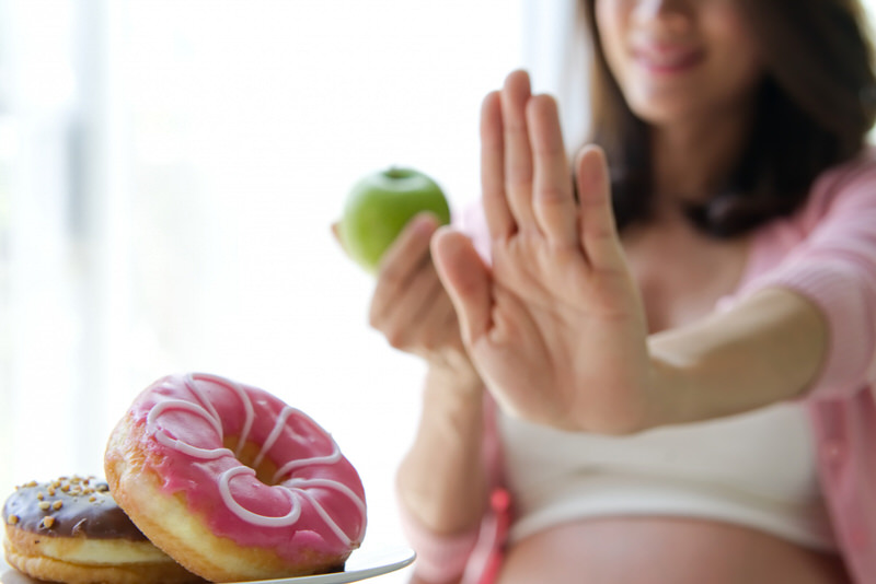 A pregnant woman is saying no to donuts and yes to an apple, so she can eat healthier for herself and her baby.