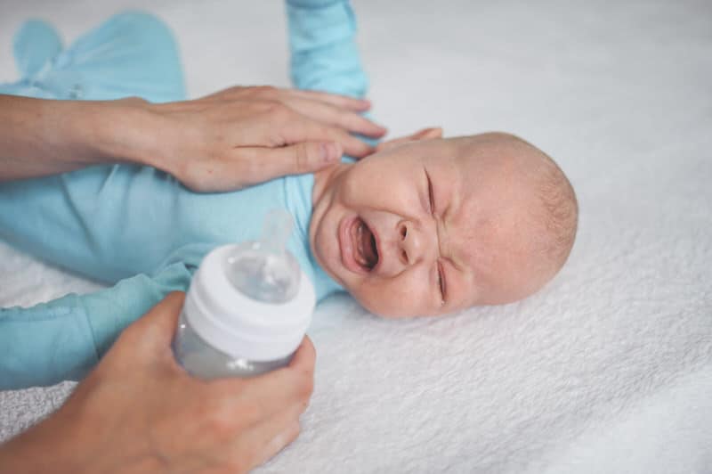 A sick newborn baby is crying and not feeling well, refusing to drink his formula milk.