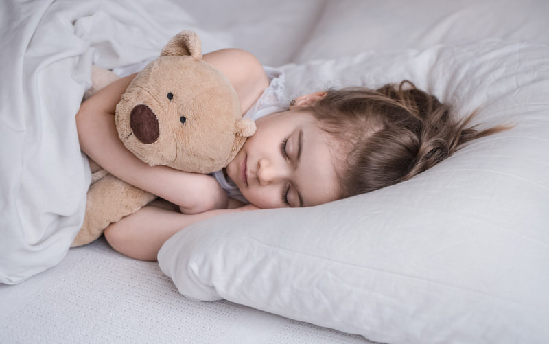 A toddler girl is sleeping in her bed with her teddy bear.