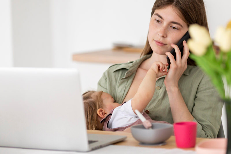 A young woman is breastfeeding her baby while working and on the phone.