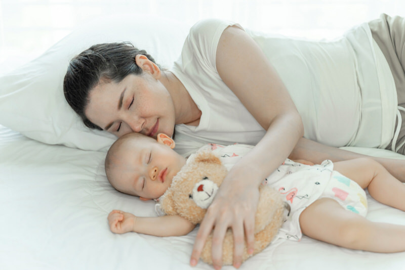 A young mom and her infant baby are sleeping. Good sleep for mom will help keep her breastmilk levels up by being well rested.