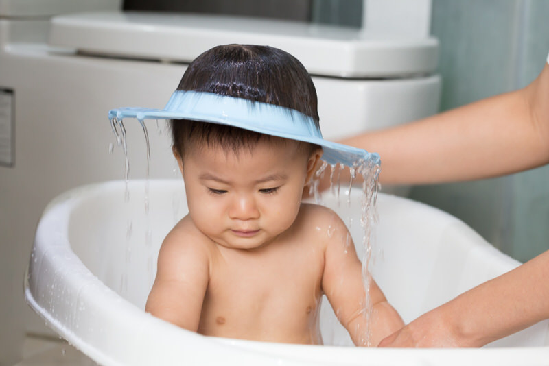 Mom is bathing her infant son and used a water shield to prevent water from getting in his face and ears.