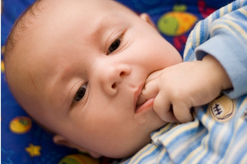 A teething 6-month infant boy is biting on 2 of his fingers and drooling.