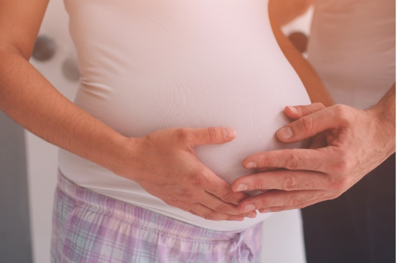 A pregnant woman and her spouse are both touching her belly because the baby has been kicking a lot.