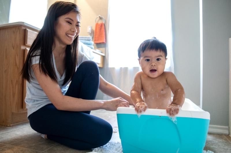 Mom is giving her infant son a nice warm bath in his infant tub in the bathroom.