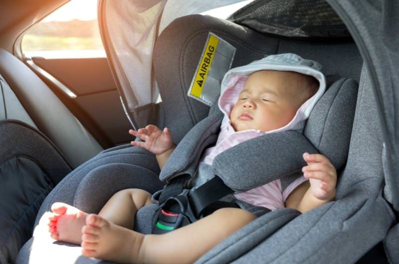 A newborn baby is sleeping in a car seat while traveling with his parents.