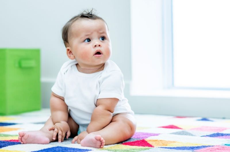 An infant boy is sitting up on a playmat at daycare.