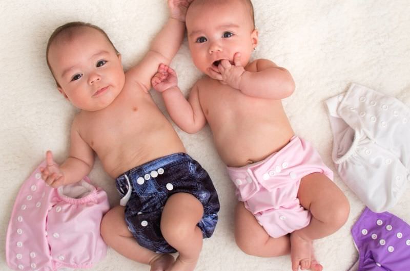Two infant babies are laying down wearing cloth diapers.