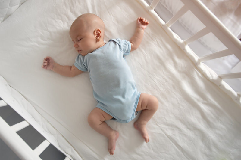 An infant boy is sleeping on his back in the crib, with no blanket