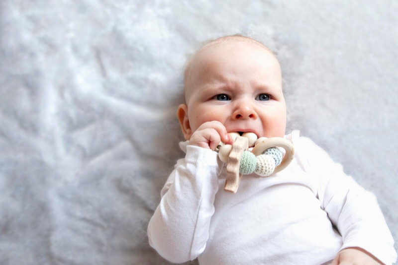 A teething infant boy is chewing on a toy to relieve pain in his gums