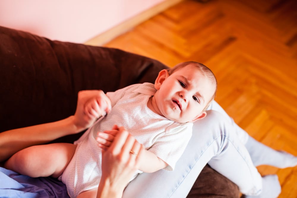 A mom is massaging her infant son after a recent feeding to help with gas and colic