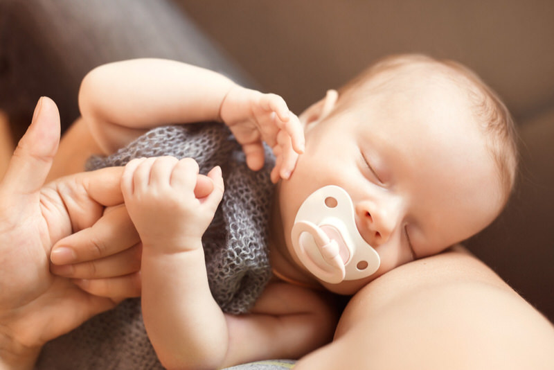 A newborn baby girl is soothing herself to sleep with a pacifier
