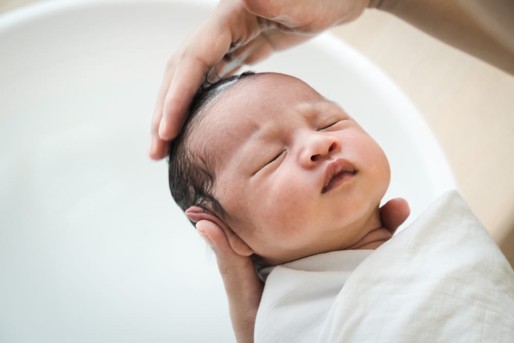 A new mom is gently shampooing her newborn baby's hair