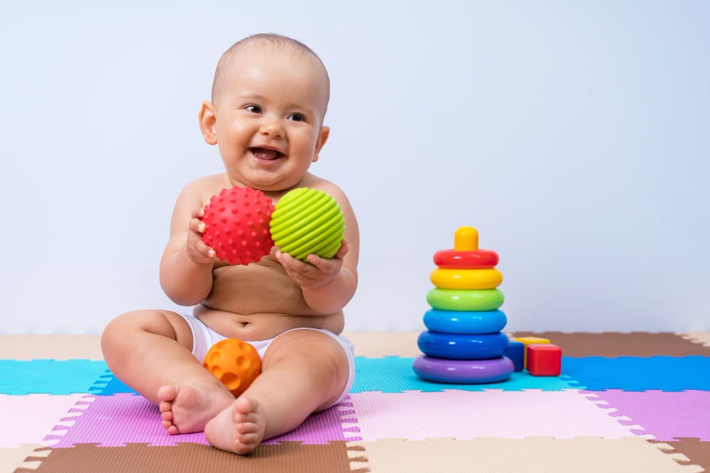 A happy infant is sitting on a play mat playing with his toys