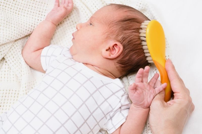 Mom is brushing her newborn baby's hair to maintain a healthy scalp