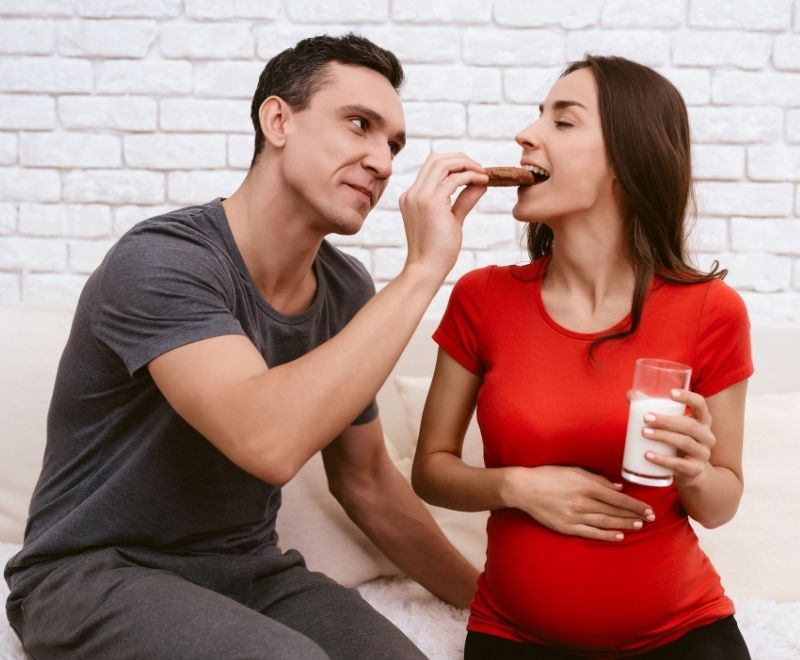 A husband is feeding his pregnant wife a lactation cookie