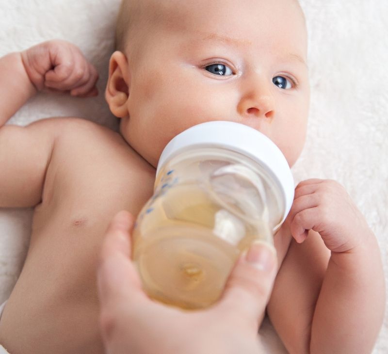 Mom is bottle-feeding her newborn son some apple juice to help with his constipation